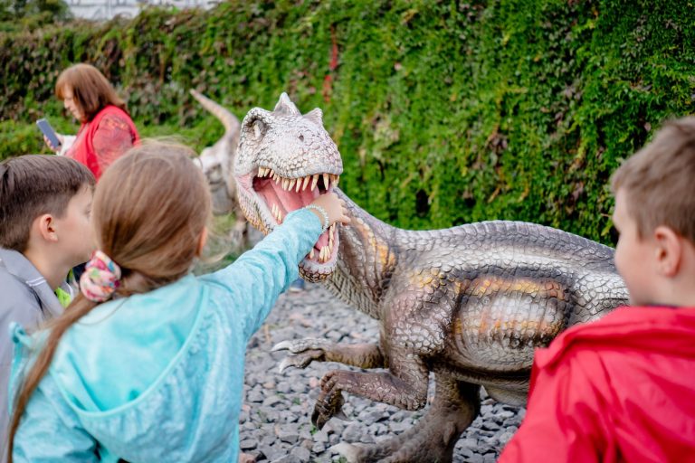 Dzieci oglądają realistyczny model dinozaura w muzeum na świeżym powietrzu