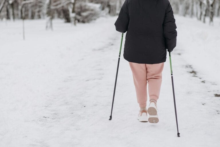 Osoba idąca po zaśnieżonej ścieżce z kijami trekkingowymi